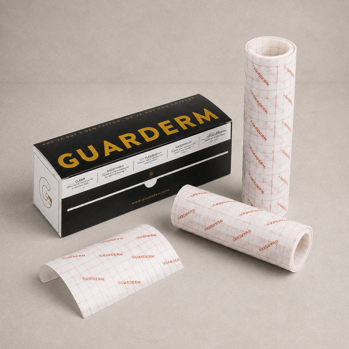 GUARDERM brand adhesive film rolls and packaging on a neutral beige background. The image shows the black and gold product box alongside two rolls of white adhesive film with a red grid pattern, and one loose strip of the film.