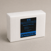 A white rectangular block of ribbed disposable pillow case material with a black and blue ARROW product label, photographed on a plain warm beige background.
