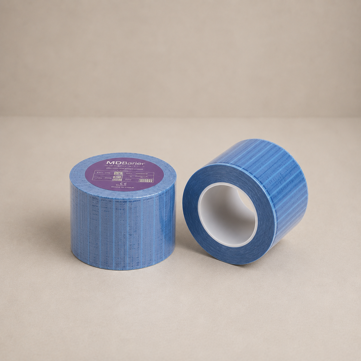 Two rolls of blue duct tape on a neutral beige background, with one roll standing upright showing a purple brand label and the other lying on its side.