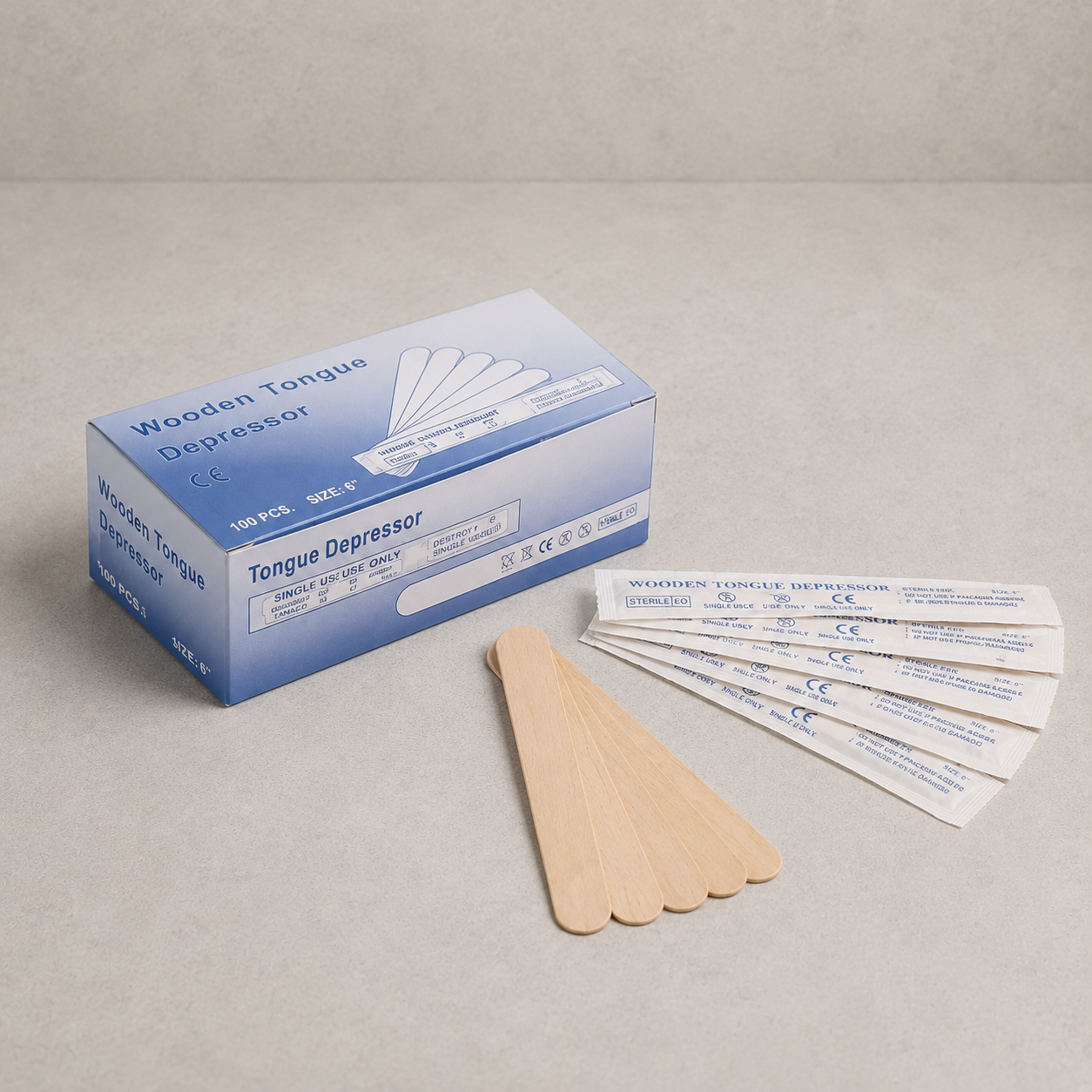 A box of wooden tongue depressors with several wooden sticks and five individually wrapped sticks displayed on a neutral beige surface.